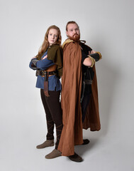 Full length  portrait of red haired  couple, man and woman wearing medieval viking inspired fantasy costumes, standing pose, isolated on white  studio background. 