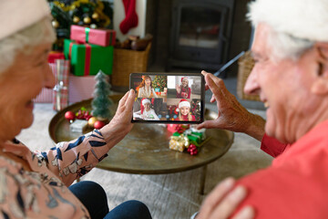 Caucasian senior couple in santa hats on christmas video call on tablet with friends and family