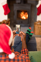 African american man in santa hat on christmas video call on smartphone with senior couple