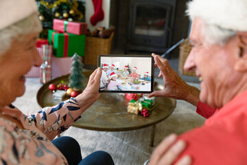Caucasian senior couple in santa hats on christmas video call on tablet with family