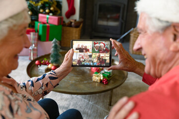 Caucasian senior couple in santa hats on christmas video call on tablet with friends and family