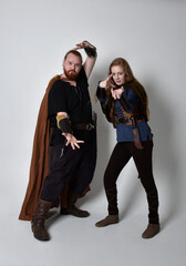 Fototapeta na wymiar Full length portrait of red haired couple, man and woman wearing medieval viking inspired fantasy costumes, standing pose, isolated on white studio background. 