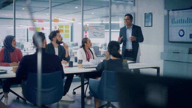 Multi-Ethnic Office Conference Room. CEO does Presentation for Diverse Entrepreneurs, Talking, Using TV with Infographics, Statistics, Graphs. Businesspeople Invest in e-Commerce Startup