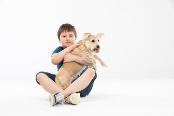 A young boy sits on a white background and in his hands he holds his beloved dog.