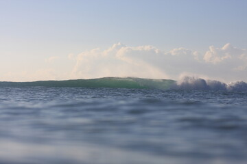 water photo of empty wave breaking in the distance with calm water in foreground and clouds in the sky