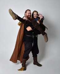Fototapeta premium Full length portrait of red haired couple, man and woman wearing medieval viking inspired fantasy costumes, standing pose, isolated on white studio background. 