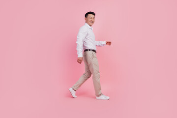 Full body profile side photo of young asian man good mood go walk isolated over pink color...