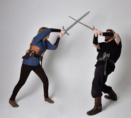 Fototapeta na wymiar Full length portrait of red haired couple, man and woman wearing medieval viking inspired fantasy costumes, standing fighting pose holding sword weapons, isolated on white studio background.