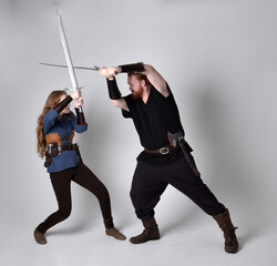 Fototapeta na wymiar Full length portrait of red haired couple, man and woman wearing medieval viking inspired fantasy costumes, standing fighting pose holding sword weapons, isolated on white studio background.