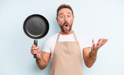 middle age handsome man amazed, shocked and astonished with an unbelievable surprise. frying pan...
