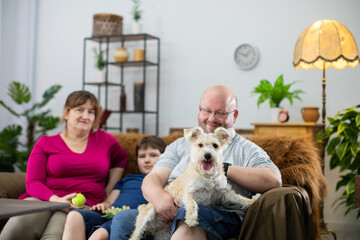 The dog sits on the lap of the head of the family and stares intently into the camera.
