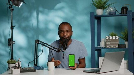 Influencer holding smartphone with green screen on display while filming video for podcast channel. Blogger using phone with isolated background and mockup template for social media vlog