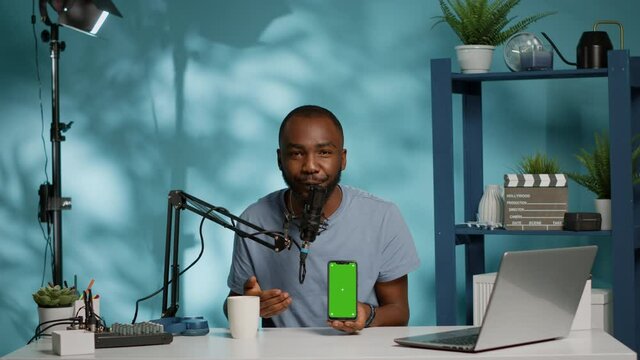 Influencer holding smartphone with green screen on display while filming video for podcast channel. Blogger using phone with isolated background and mockup template for social media vlog