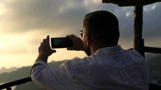 Man taking cellphone photo of Ha Long Bay in Vietnam during sunset