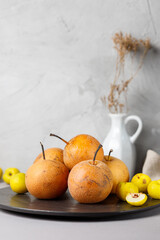 Still life with nashi pears and quince on a black plate. Vertical on a gray background
