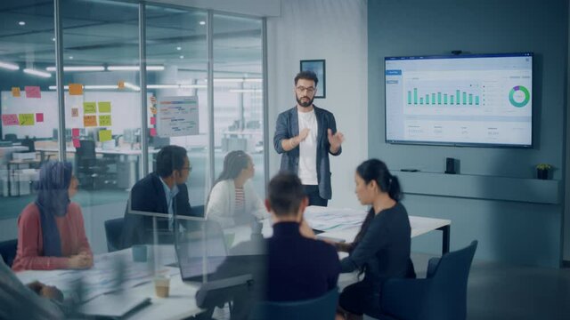 Diverse Modern Office: Motivated Businessman Leads Business Meeting with Managers, Talks, uses Presentation TV with Statistics, Chart Growth, Big Data. Digital Entrepreneurs Work on e-Commerce Project