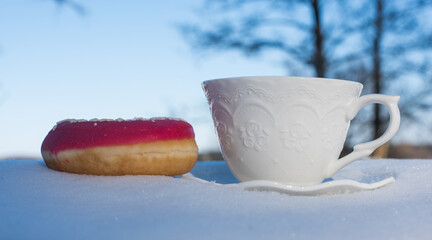 Cup of tea for breakfast with donuts on snow background