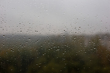 Window with raindrops and blurry view of the autumn forest