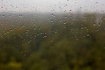 Window with raindrops and blurry view of the autumn forest