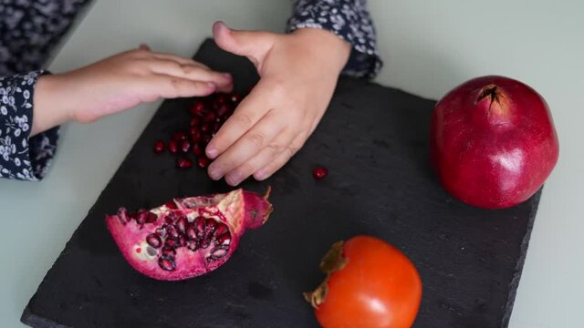 Adorable little girl touching pomegranate seeds in a healthy and healthy snack sitting in the kitchen at home. Autumn fruits. Vegan and healthy elements for dessert and snack for children.