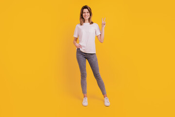 Fototapeta na wymiar Photo of friendly positive lady show v-sign gesture wear casual t-shirt jeans on yellow background