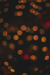 vertical photography of unfocused bokeh lights with yellow illumination from garland lamps on black background space, New Year and Christmas concept