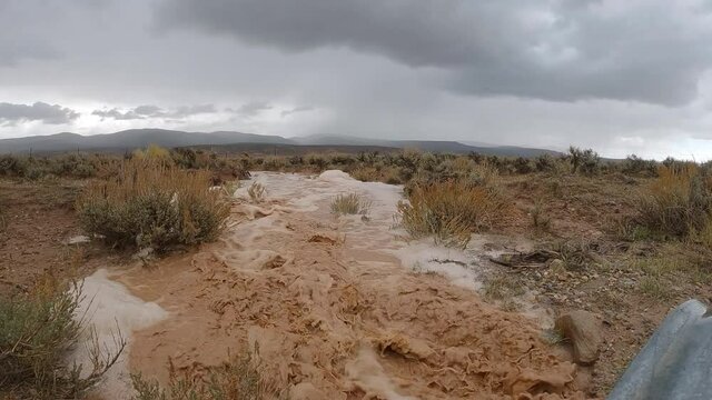 Muddy flood water moving over the landscape during heavy rainstorm in slow motion.