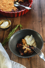 Homemade plum crumble pie with whipped cream on wooden table. Selective focus