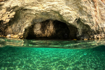 Underwater split photo of small white rock cave with crystal clear emerald sea and chapel of Agios Nikolaos built inside the cave, Desimi beach, Lefkada island, Ionian, Greece
