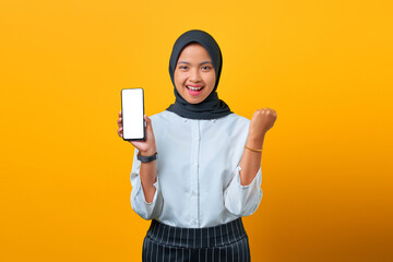 Happy Asian woman showing mobile phone blank screen and hand gesture success on yellow background