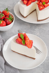 No baked cheesecake with fresh strawberries and mint on top on a white plate on a gray concrete background. Copy space.