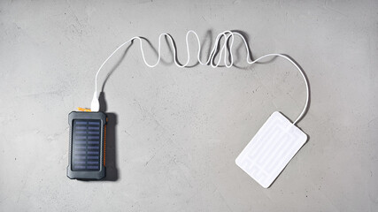 Portable heater is connected by wire with USB to connector power bank with solar panel on gray textural background with copy space