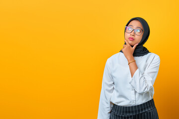 Pensive young Asian woman looks seriously thinking about a question on yellow background