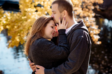 Beautiful young couple man and woman hugging in the park near the pond in leaf fall in autumn