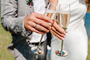 The bride and groom holds a glass of champagne and stand on nature at the wedding ceremony. Close up. Holiday. Look at the glasses.