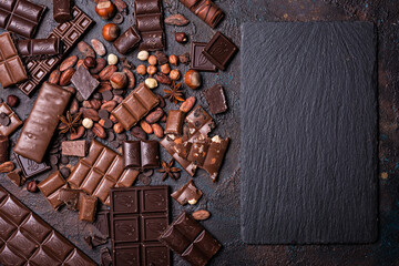 Chocolate background with slate board and lots of bars, nuts, cocoa beans