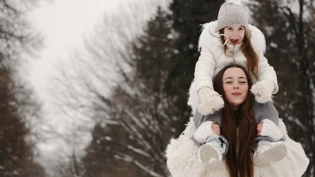 Mother carrying daughter on shoulders below trees in winter wood