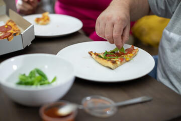 A man puts a green arugula leaf on a slice of pizza.
