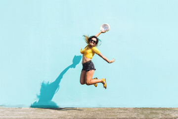 Hispanic girl jumping with excitement and happiness in front of a blue wall.