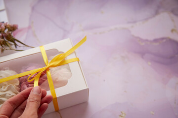 Woman hands giving a present box with pink and white marshmallow close up. Boxing day concept. Cozy winter weekends. Homemade sweets