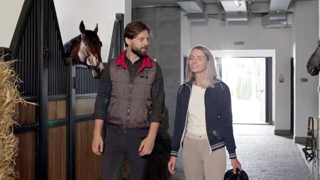 Full length view of the confident man and woman chatting with each other after taking care of the horses while working at the stable together. Occupation concept