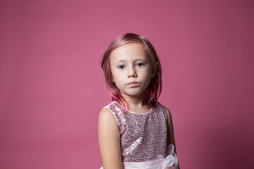 Little caucasian girl in a festive dress with sequins posing on pink backdrop