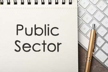 Notebook with phrase PUBLIC SECTOR and keyboard on table, flat lay