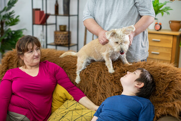 The father stands behind the sofa and strokes the shaggy dog the rest of the family watches all the fun.