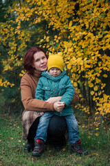 Fototapeta premium Little caucasian boy and his mother against yellow autumn forest