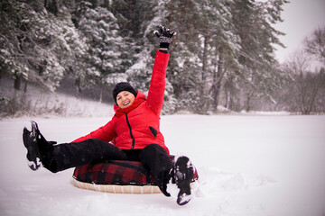 a girl in a red jacket rides a tubig in a snowy forest and laughs.
