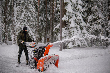 a man removes snow with a snowblower on the background of a snowy forest.