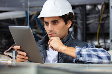 technician in safety helmet holding digital tablet