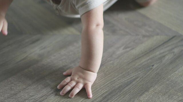close-up tiny little hands fingers of caucasian baby infant touching beating crawling on the wooden floor at home. kid trying to move crawl first time palm and feet on the parquet living room daytime