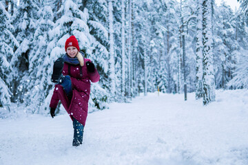 Fototapeta na wymiar teenage girl in a red jacket kick the snow and laughing in a snowy forest